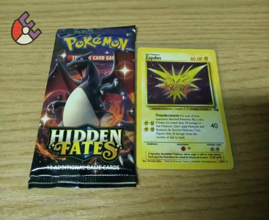 A photo showing a sealed Pokémon booster pack labeled 'Hidden Fates' and a vintage Pokémon card lying in front of it.